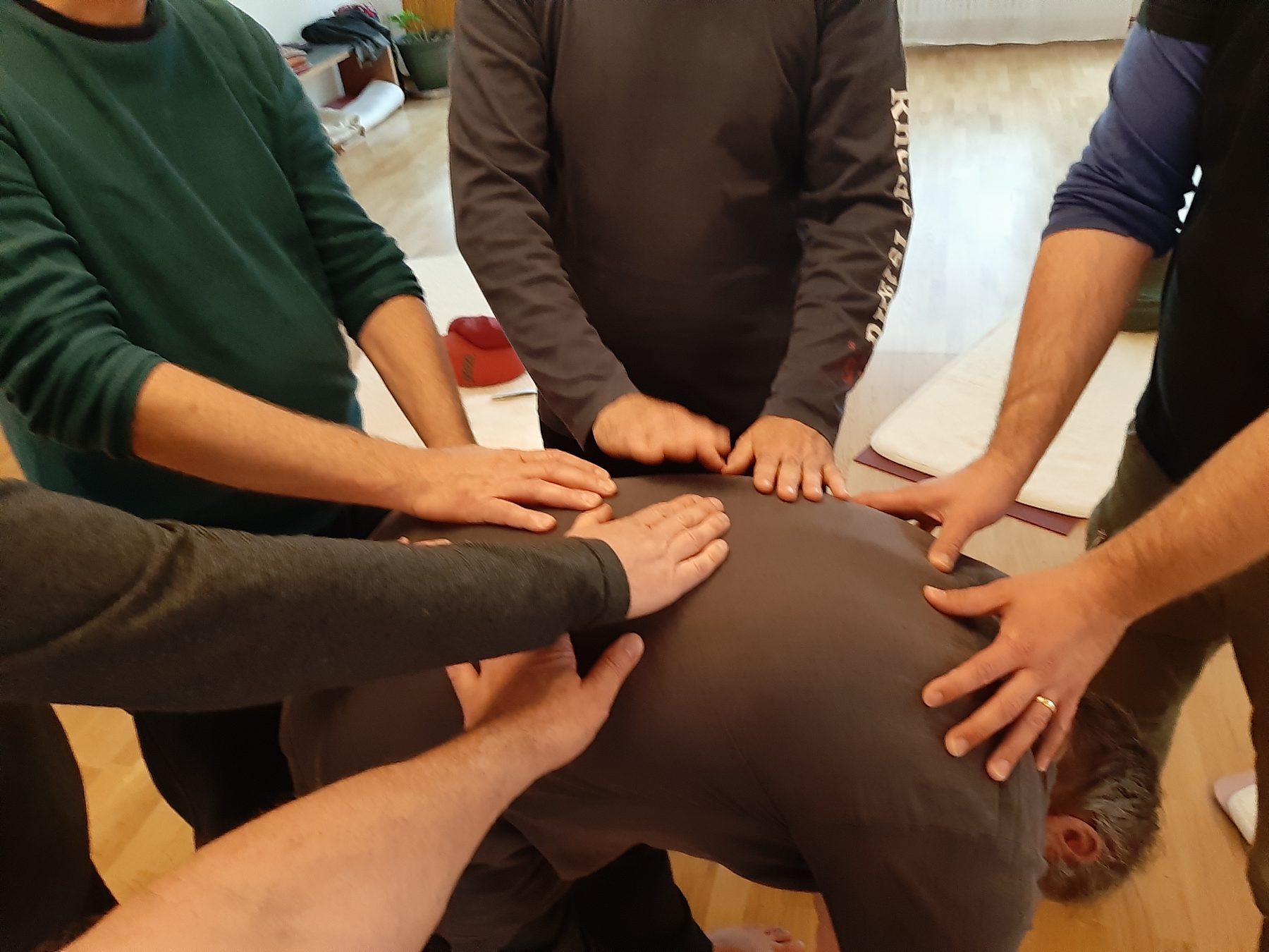 Mehrere Männer legen einem knienden Mann die Hände auf den Rücken