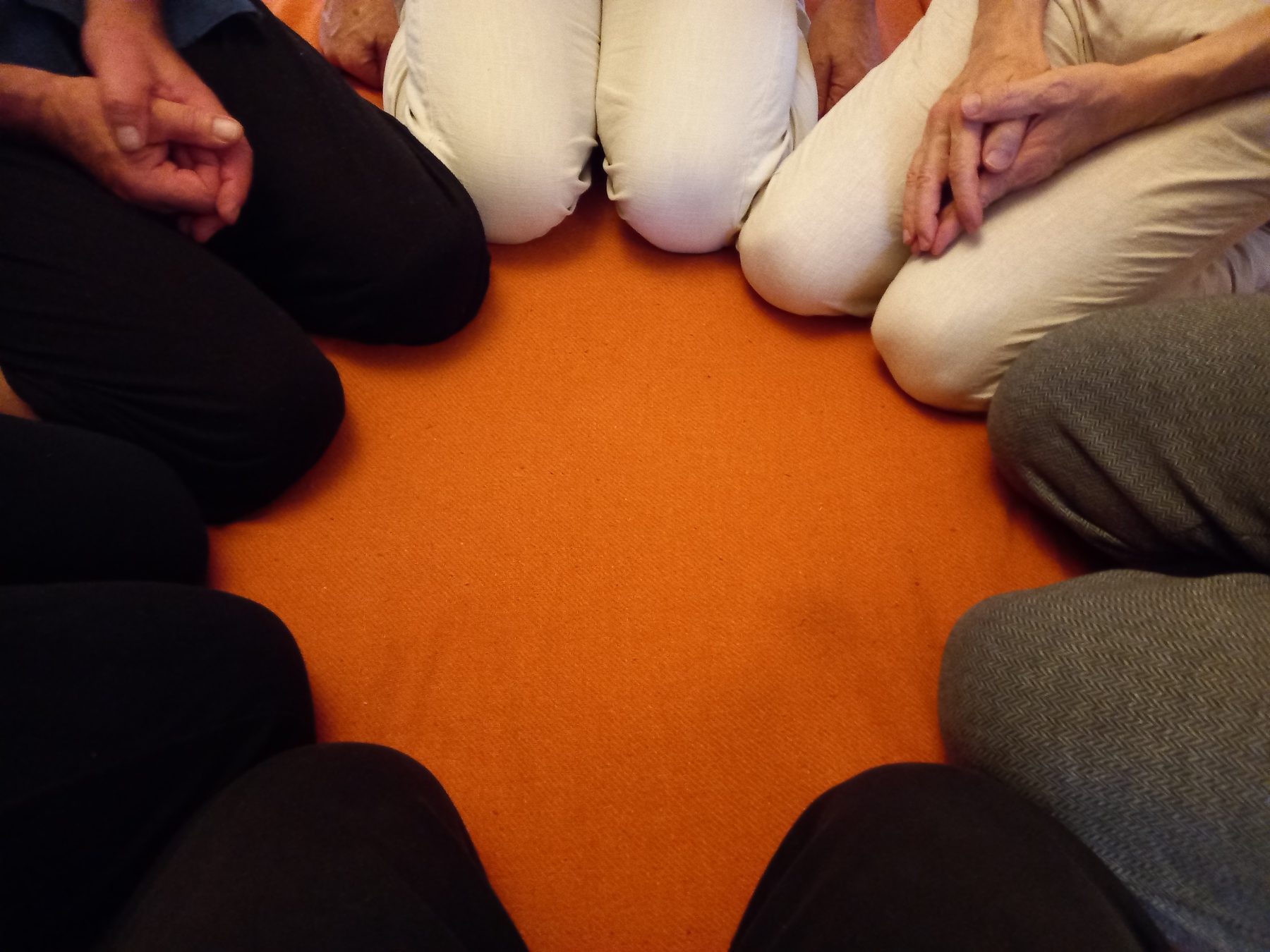 Männer sitzen im Kreis auf dem Boden um einen orangefarbenen Teppich